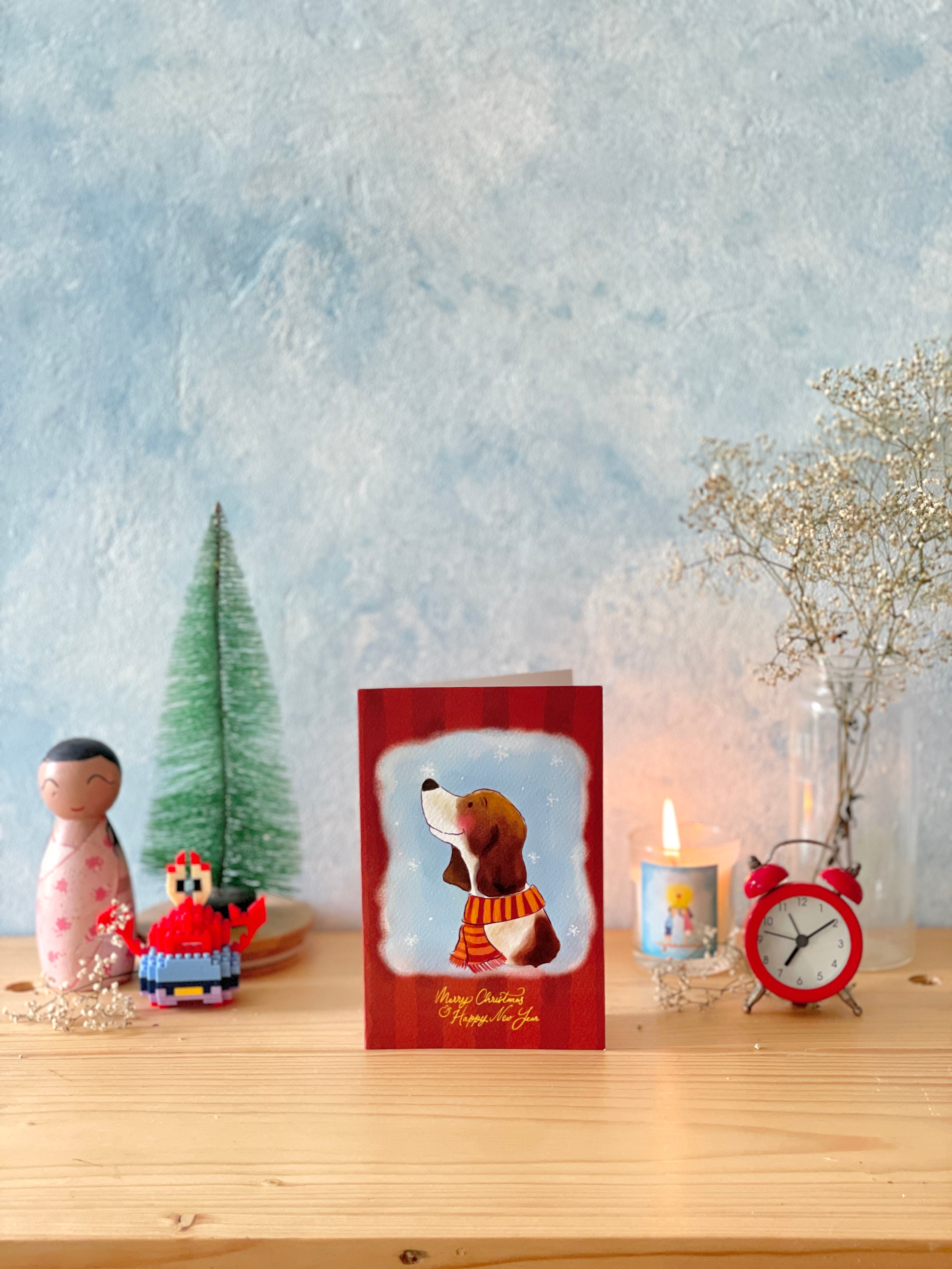 Christmas card with a dog illustration on a table with decorative items.